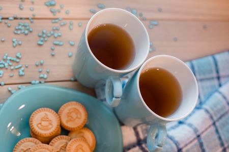 Two cups of tea on a blue linen napkin. Biscuits on a blue plate on a wooden backgroundの写真素材