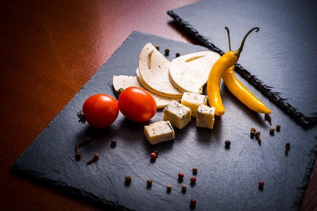 Cheese with mold, cherry tomatoes, basil and melissa greens, red and yellow hot pepper on a stone tray on a dark gray backgroundの写真素材