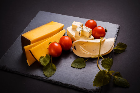 Cheese with mold, cherry tomatoes, basil and melissa greens, red and yellow hot pepper on a stone...