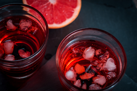 Grapefruit lemonade and cola glass with ice cubes and droplets. On a dark gray background on a stone tray, cut fresh fruit close-upの写真素材