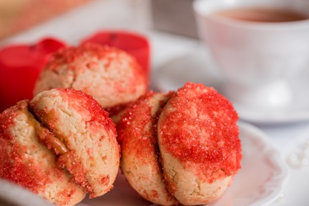 Cookies with strawberry cream covered with sprinkles, Red round cookies on a tray, cup of tea on wooden background, valentine, valentine dayの写真素材