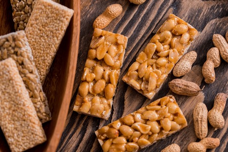 Snacks - mix of energy bars with peanut, sesame and sunflower seeds on a wooden background. Nuts in caramel, honey Snack food. Unhealthy eating or a healthyの写真素材