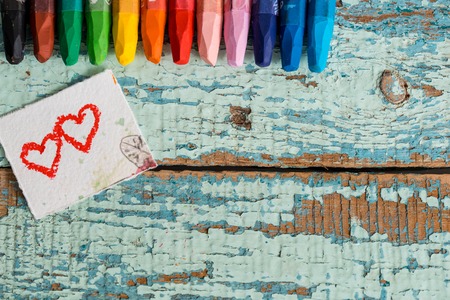 Colored pencils on lilac background. Wooden pencils lie on the lilac surface. Bright colored pencils on an old blue green wooden background. Two red hearts painted on a slice of paperの写真素材