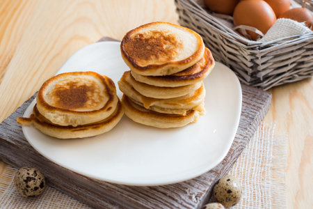 Stack of pancakes in white saucer on light wooden table, On a white plate