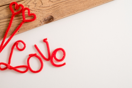 Love is a word is written spelling font. The word love red. White background, wooden table. Copy space. Place for your inscriptionの写真素材
