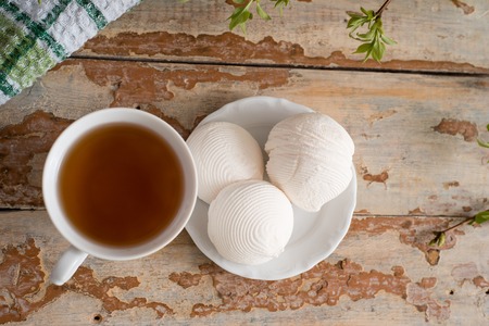 Beautiful composition with cup of tea and marshmallow. Spring Breakfast. A cup of tea with a white marshmallow on a wooden background. Sprigs of a tree with green buds and leaves.の写真素材