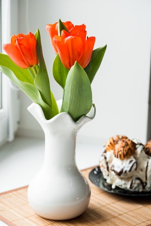 red tulips in a white vase, Easter cake, spring baking cake on a black plate. on the tableの写真素材