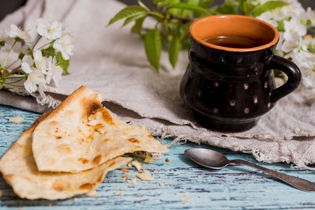 Tea in an old mug, thin cake pastry next, cherry blossoms on a blue wooden background close-up. wabi sabi seriesの写真素材