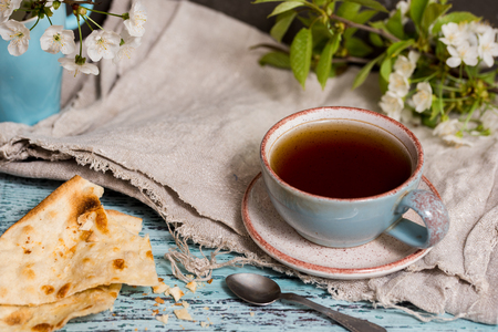 Tea in an old mug, thin cake pastry next, cherry blossoms on a blue wooden background close-up. wabi sabi seriesの写真素材