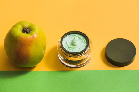 a face cream, a green apple, a yellow daisy on a bright background.Natural cosmetics with fresh flowers in an open jarの写真素材