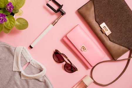 clothes, a purse and a bag, a comb and sunglasses, a self-stick and eau de toilette. Flowers are next to a pink background. Fashion trends of summer for the women. Flat lay, top view. Copy spaceの写真素材