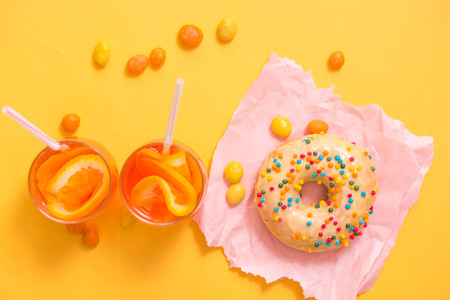 Female hand holding donut with sprinkles on yellow background.の写真素材