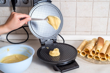 Making waffles at home - waffle iron, batter in bowl and ingredients - milk, eggs and flour. Cooking...