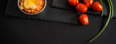 Appetizing meat with mushrooms, baked with cheese in a coconut, two small portions in an iron bowlnear cherry tomatoes . Against a dark background. With copy space. Healthy eating concept. Long wide banner.の写真素材