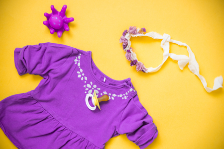 Baby Purple clothes and necessities on yellow background. A dummy and a wreath a bandage on the headの写真素材