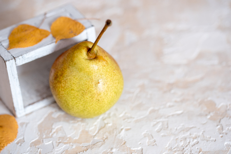 Autumn pear in a white old wooden small box. Life style. Yellow autumn leaves on a concrete light background. Selective focus, space for text.の写真素材