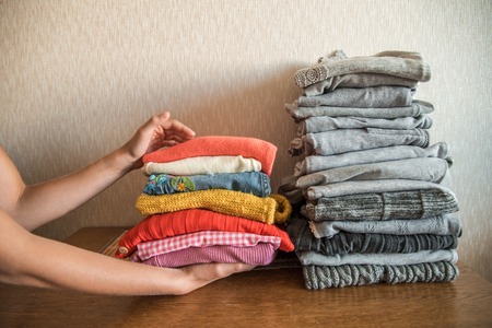 Red orange and yellow bright stack of clothes against the gray. The concept of choice and individuality. The hands of the girl take colorful clothesの写真素材