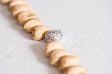 a strip of pistachios on a white background. one pistachio of a different color. silver paint. The...