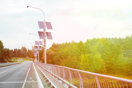 Street lamp poles powered by solar energy. Solar panels on electric pole for lighting on the road in the city on the bridge. Use of solar energyの写真素材
