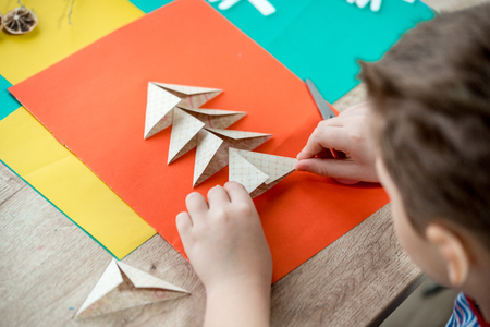 Child's hands cutting colored red paper with scissors . Christmas tree made of colored paperの写真素材