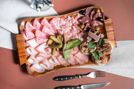 Meat appetizer selection or wine snack set. Variety of smoked meat, salami, prosciutto, bread sticks, baguette, olives and sun-dried tomatoes on rustic wooden board, top viewの写真素材