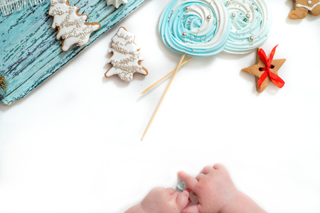 Baby hands, Christmas gingerbread and meringue, sweet candy on a stick on a blue board and a white background, Christmas card. top view, Flat layの写真素材