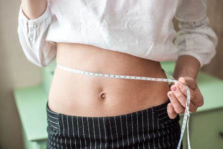 Closeup asian woman holding salad vegetable food and measuring waist for weight isolated on white background, girl diet with cellulite loss with tape measure, health care or wellness concept.の写真素材