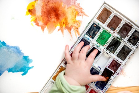 little girl bedaubed with bright colors. Multicolored watercolor in small hands. Blot on white backgroundの写真素材