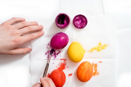 Closeup human hand painting easter egg with paintbrush. Yellow, orange, red and purple eggの写真素材