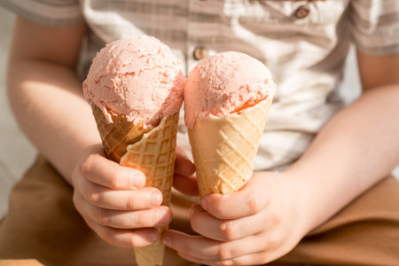 ice cream in the hands of a child. A happy boy is holding two pink ice cream cones in a waffle cup....