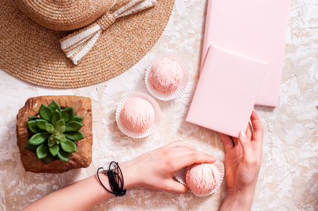 strawberry ice cream on a light background, the concept of summer, straw hat, pink notebook, women's summer accessories, hands girls take ice cream and mobile phoneの写真素材
