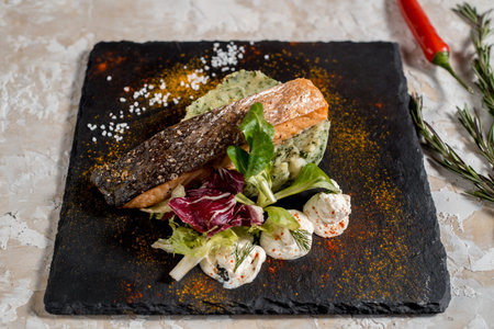 Roasted salmon fish steak with potato, sauce in white plate on dark background