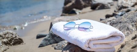 Long banner sunglasses lying on tropical sand beach. white towel and glasses with seashells. Sunglasses on the beach. Beautiful sea view wallpaper, background.の写真素材