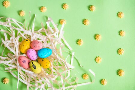 colored bright easter eggs in a nest on a green paper background. easter card.Flat lay.Copy space.Sweet yellow sweets. patternの写真素材