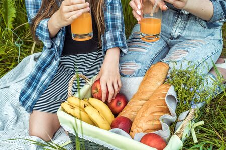 Outdoors park picnic. Beautiful young mom and little girl sitting in forest and enjoying.white bread, pastries, fruits in basket, apples and bananas.Drink orange juice from glass from straw. mustacheの写真素材