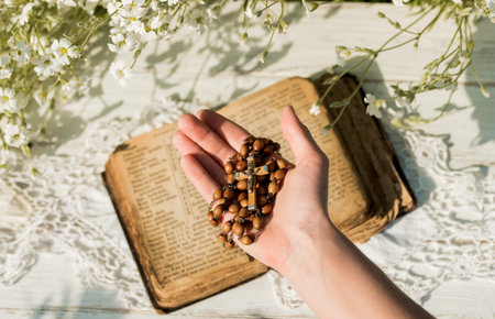 Hands folded in prayer over old Holy Bible. Wooden background.Hands and rosary, prayer, old book with yellow pages. white flowers on a background. in the garden. Concept of prayer and religion.の写真素材