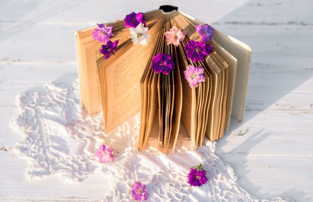 Violet flowers gelichrysum on a book. openwork knitted tablecloth on a wooden old table. evening in...