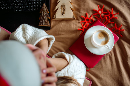 Winter holidays morning. Woman having breakfast with cup of coffee latte in hands in bed. Coziness weekend. Relaxing Sunday activities. Top view.の写真素材