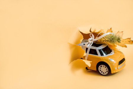 toy car bursts through torn paper, autumn on yellow paper. The concept of a cozy and modern autumn. Trend yellow background.の写真素材