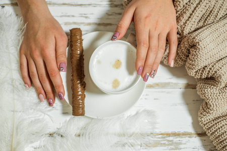 Womans hands in sweater holding cup of coffee on wooden table.chocolate on a plateの写真素材