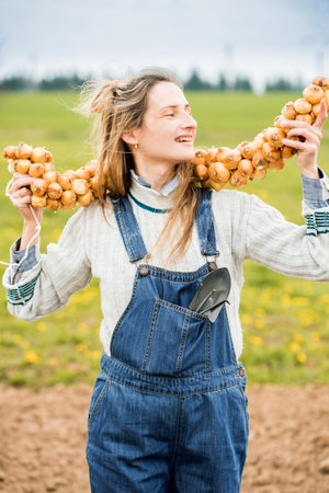 happy girl farmer in a field in denim overalls holds a bunch of onions. Planting bulbs in the ground in garden.The beds and the field. Ranch girl. Planting plants.の写真素材