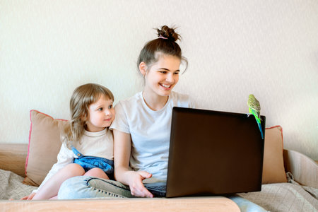 Happy children play with a parrot at the computer. Online games at home with a laptop with a pet.two baby girls and a teenager. online consultation of the vetの写真素材