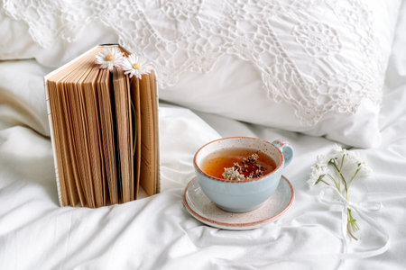 Openwork lace, cotton white blanket. book botany, mug with natural herbal tea made from mint, summer daisy flowers. Morning breakfast in bed. Provence and retro style. Clean cosiness and freshness.の写真素材