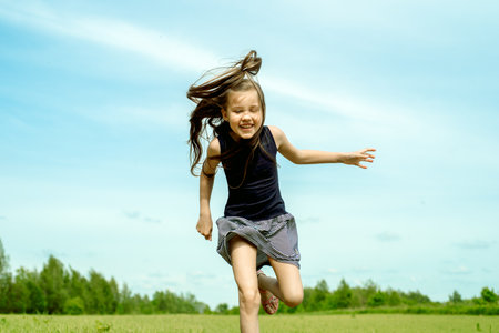 Little girl running on a meadow in a field of flowers, Summer day. barefoot jumping on the grass, happy laughs. Horizon and sky.freshness idea and freedom. happy childhoodの写真素材