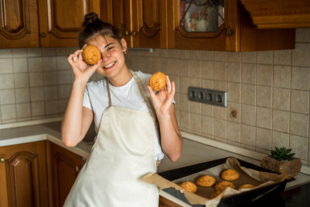 Smiling teen girl taking cookies out of the oven Homemade cakesi n the kitchen., cookies and gingerbread cookies. sweet breakfast. selective focusの写真素材