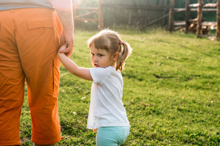 a parent holds the hand of a small child.baby girl goes hand in hand with dad in the village at sunset. sunny evening.fathers day.の写真素材