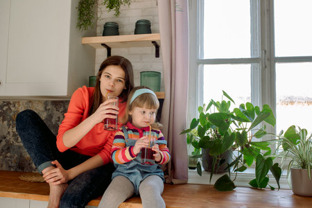 Children in the kitchen drink juice. Cute little sister girls have breakfast with fruits. Healthy nutrition. Red strawberry or cherry juice in a glass. Modern lifestyleの写真素材