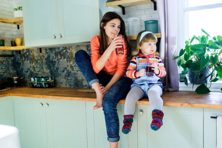 Children in the kitchen drink juice. Cute little sister girls have breakfast with fruits. Healthy nutrition. Red strawberry or cherry juice in a glass. Modern lifestyleの写真素材
