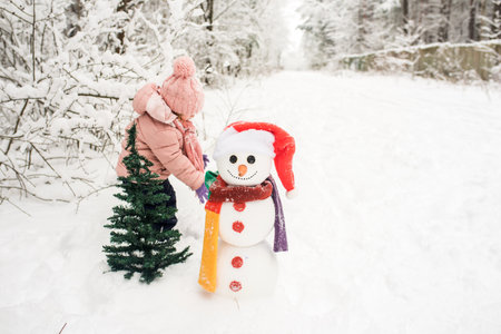 happy kid playing with snowman. funny little girl on a walk in the winter outdoorsの写真素材