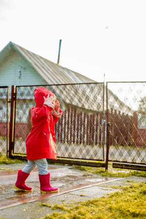 Cute girl in a red jacket is jumping in the puddle.The setting warm summer or autumn sun. summer in the village.の写真素材